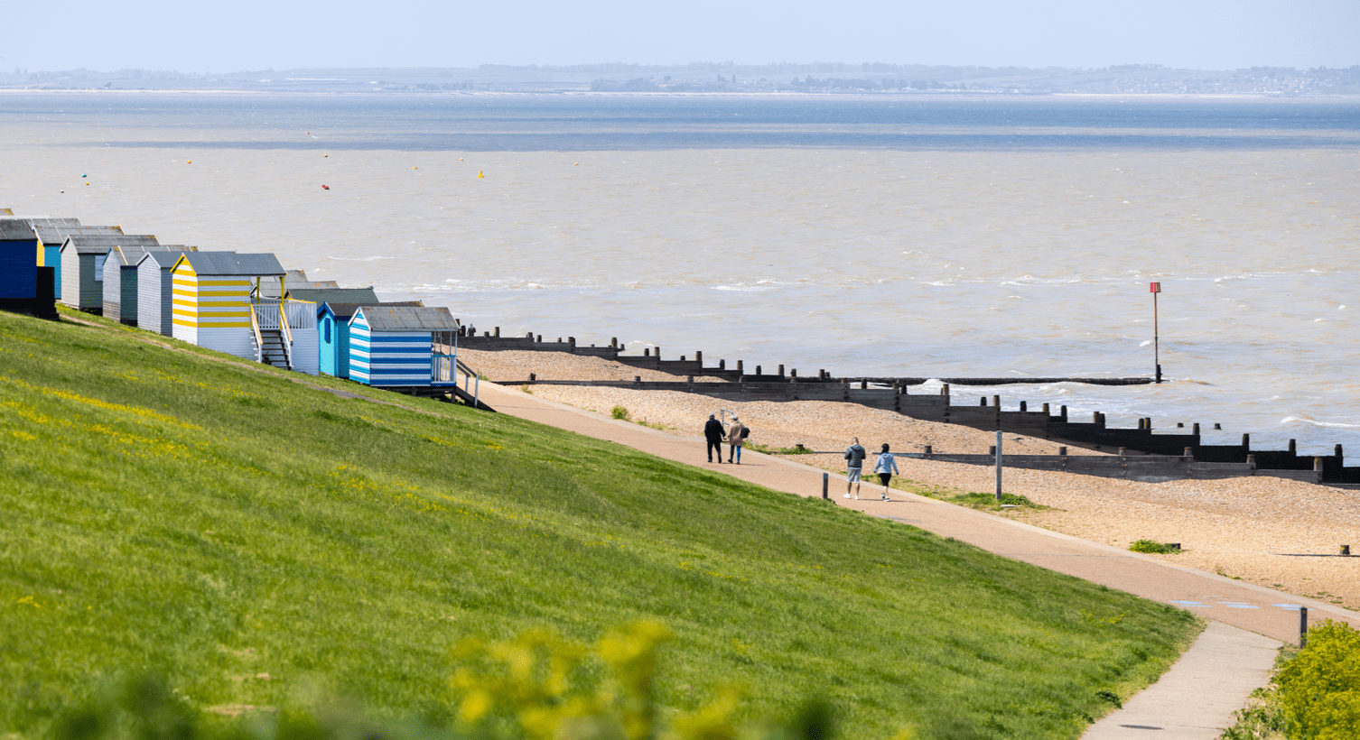 A photo of beach huts looking out onto a beach with sand groynes